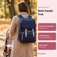 Mother walking in a park with the navy Bumpwell diaper backpack, both hands free for the stroller
