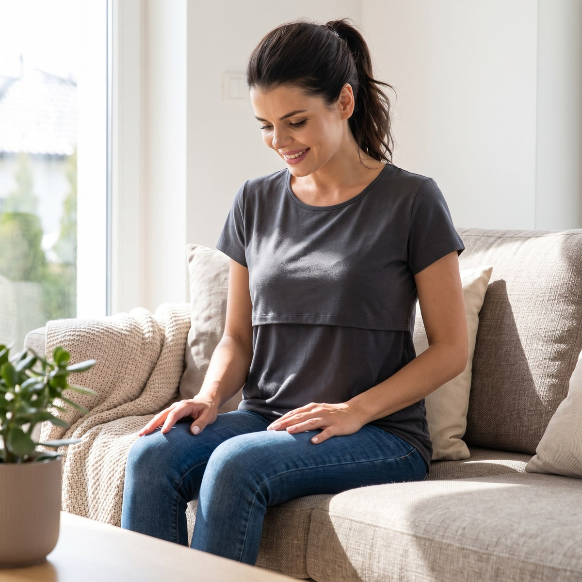 Woman sitting on a sofa in the charcoal grey Bumpwell nursing T-shirt