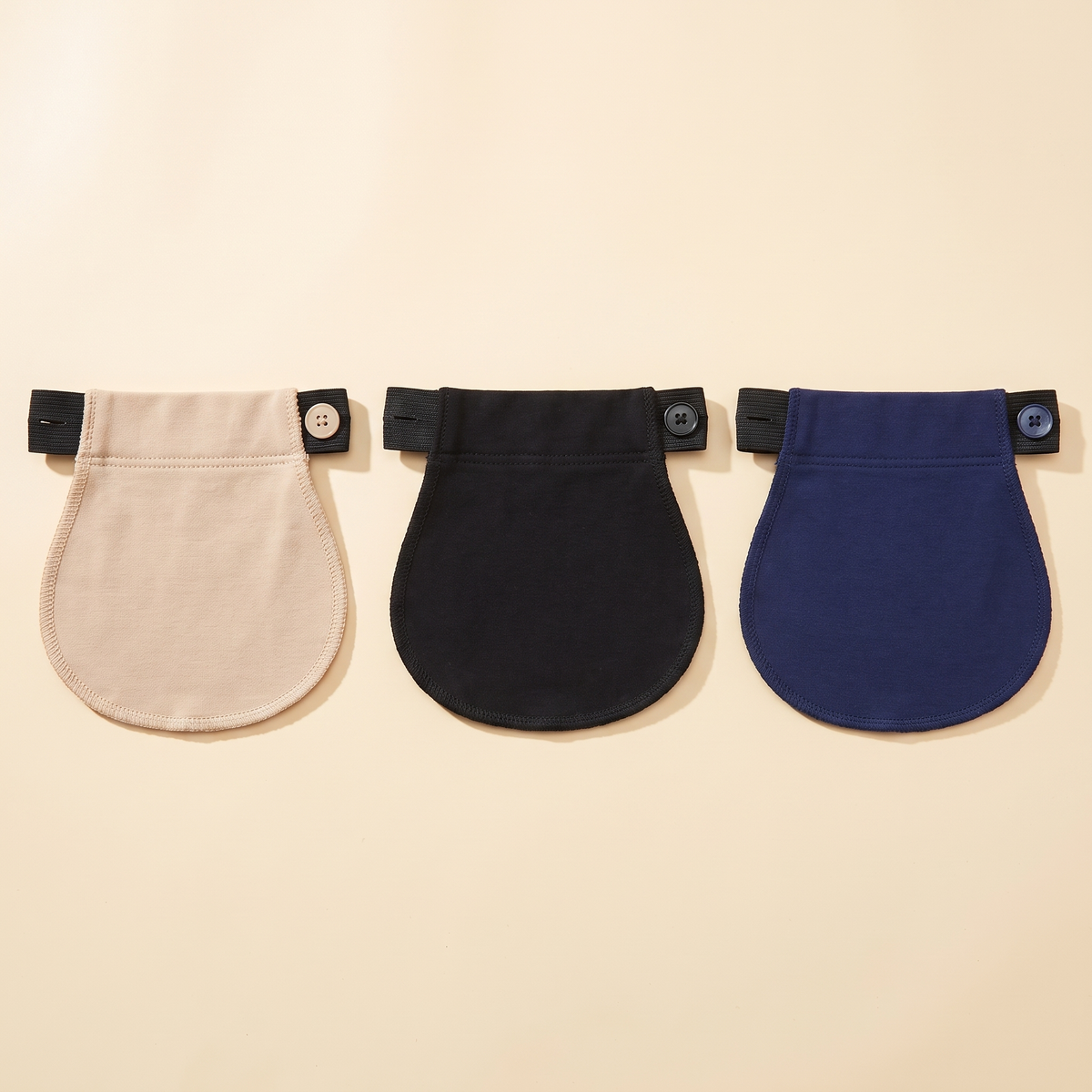 Three maternity pants extenders in beige, black and navy on a cream background