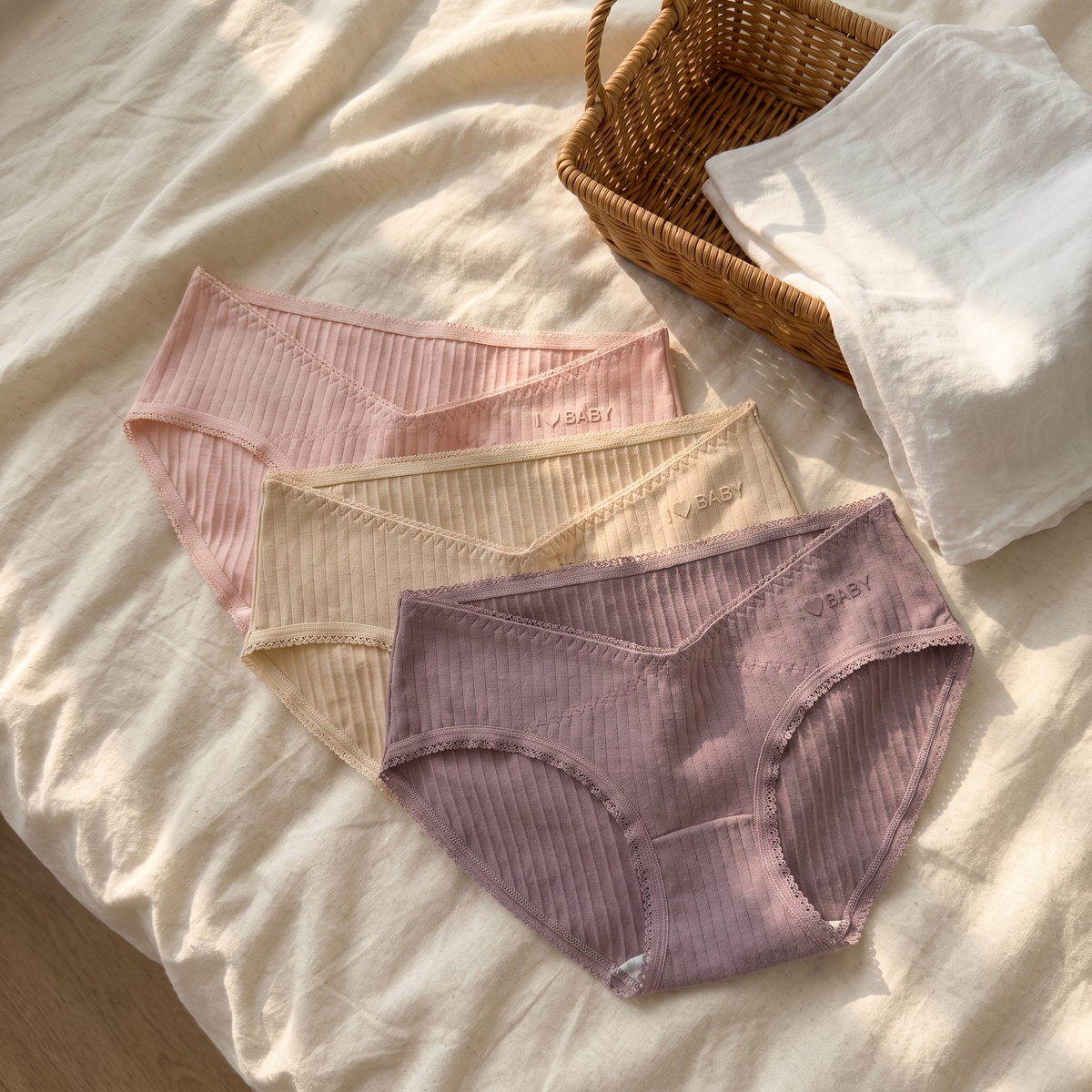 Three cotton maternity briefs in pink, beige and mauve laid on a bed