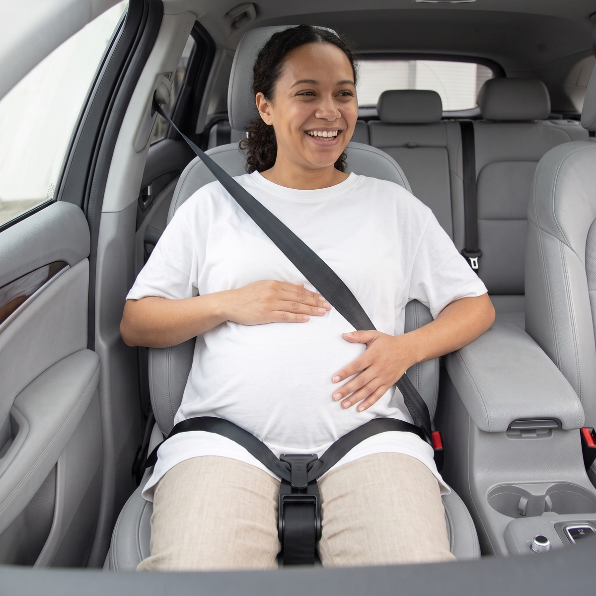 Pregnant woman smiling in the car with the lap belt held low by the Bumpwell seat belt adjuster